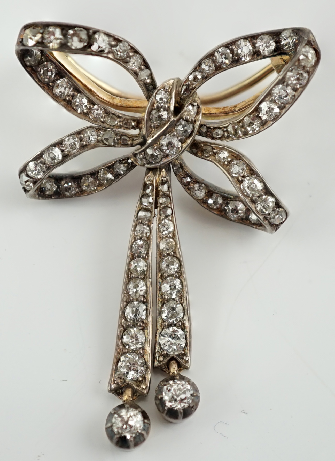 An Edwardian gold, silver and graduated diamond cluster set twin drop ribbon bow brooch